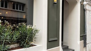 A building facade with a green door, a window with plants, and a staircase leading to an entrance. - Hôtel Hiro (Paris)