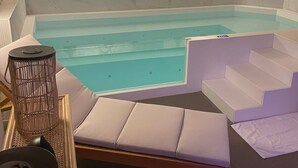 A swimming pool with a stone wall backdrop, a sunken seating area, and a staircase leading to an upper level. - Hôtel Hiro (Paris)
