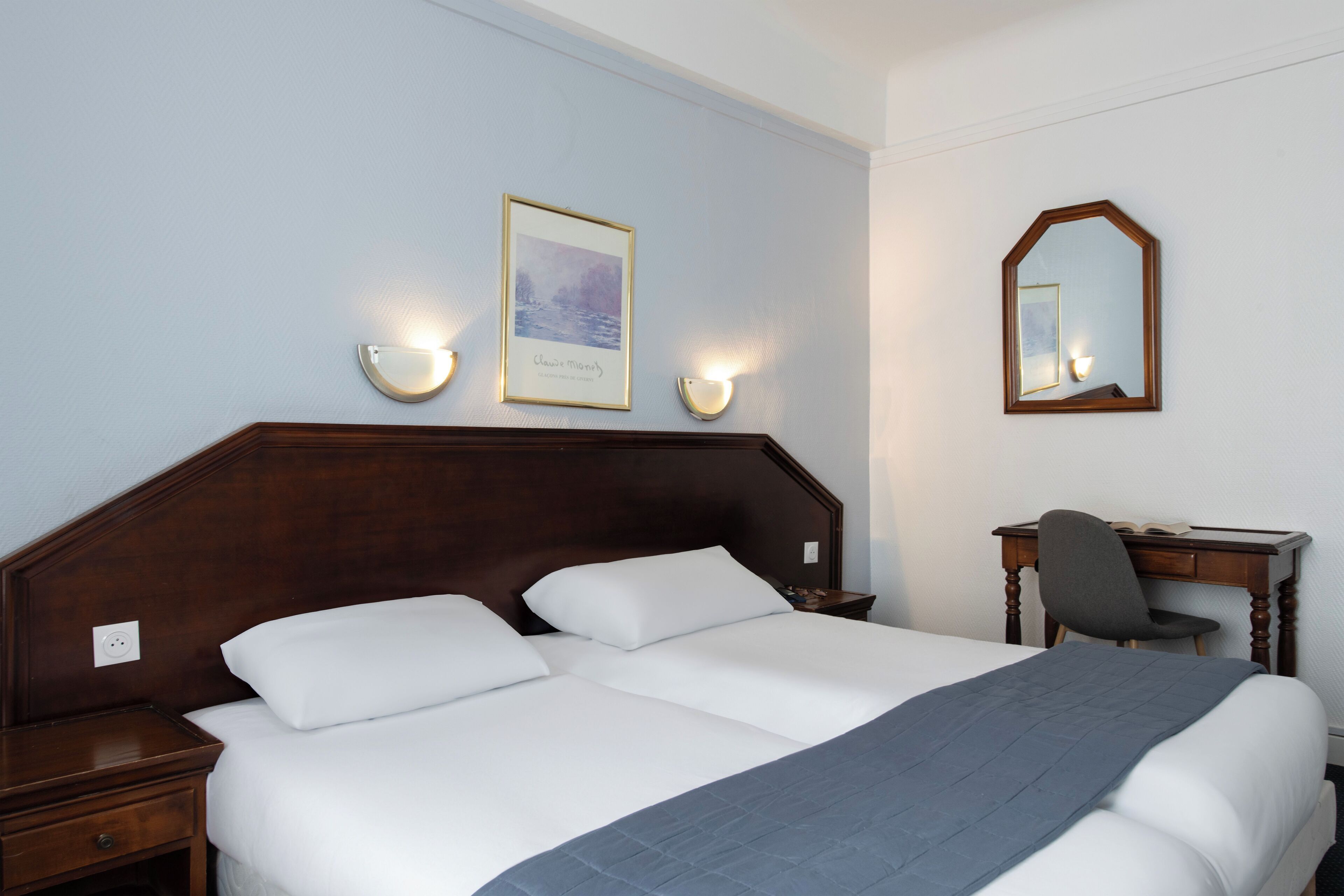 A hotel room with a large bed, bedside tables, a desk with a chair, and a mirror on the wall.