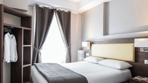 A hotel room with a large bed, a wardrobe, and a bedside table with a lamp. - Hôtel Ambassadeur (Paris)