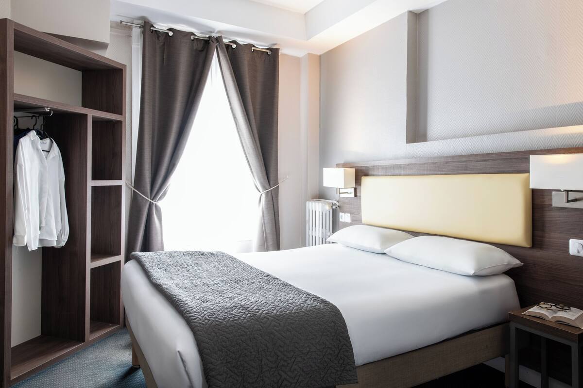 Een hotelkamer met een groot bed, een kledingkast en een nachtkastje met een lamp.