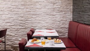A restaurant with a stone wall backdrop, red leather booth seating, and a table set with breakfast items. - Hôtel Ambassadeur (Paris)