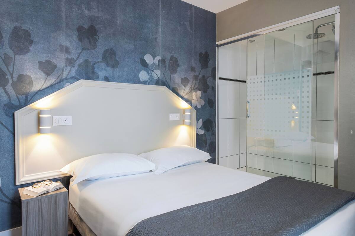 Een moderne hotelkamer met een groot bed, een nachtkastje, een douchecabine van glas en een bloemenprint behang.