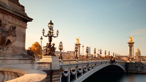 A historic bridge with ornate lamp posts and statues, spanning a river with a cityscape in the background. - Hôtel Ambassadeur (Paris)