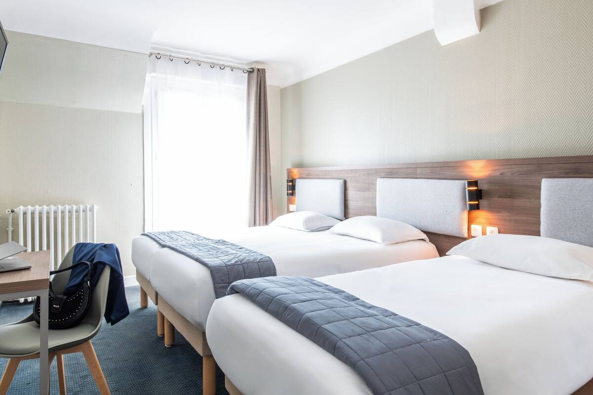 Een hotelkamer met twee bedden, een bureau, een stoel en een raam met gordijnen.