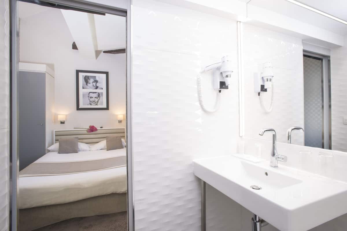 Casa de banho de hotel moderna com um espelho grande, uma pia branca e um secador de cabelo fixado na parede.