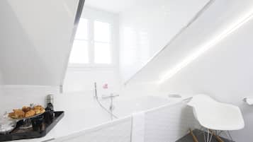 A modern bathroom with a freestanding bathtub, a white chair, and a tray of pastries.