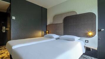 A hotel room with a large bed, a headboard with a textured pattern, a bedside table with a lamp, and a door with a handle.