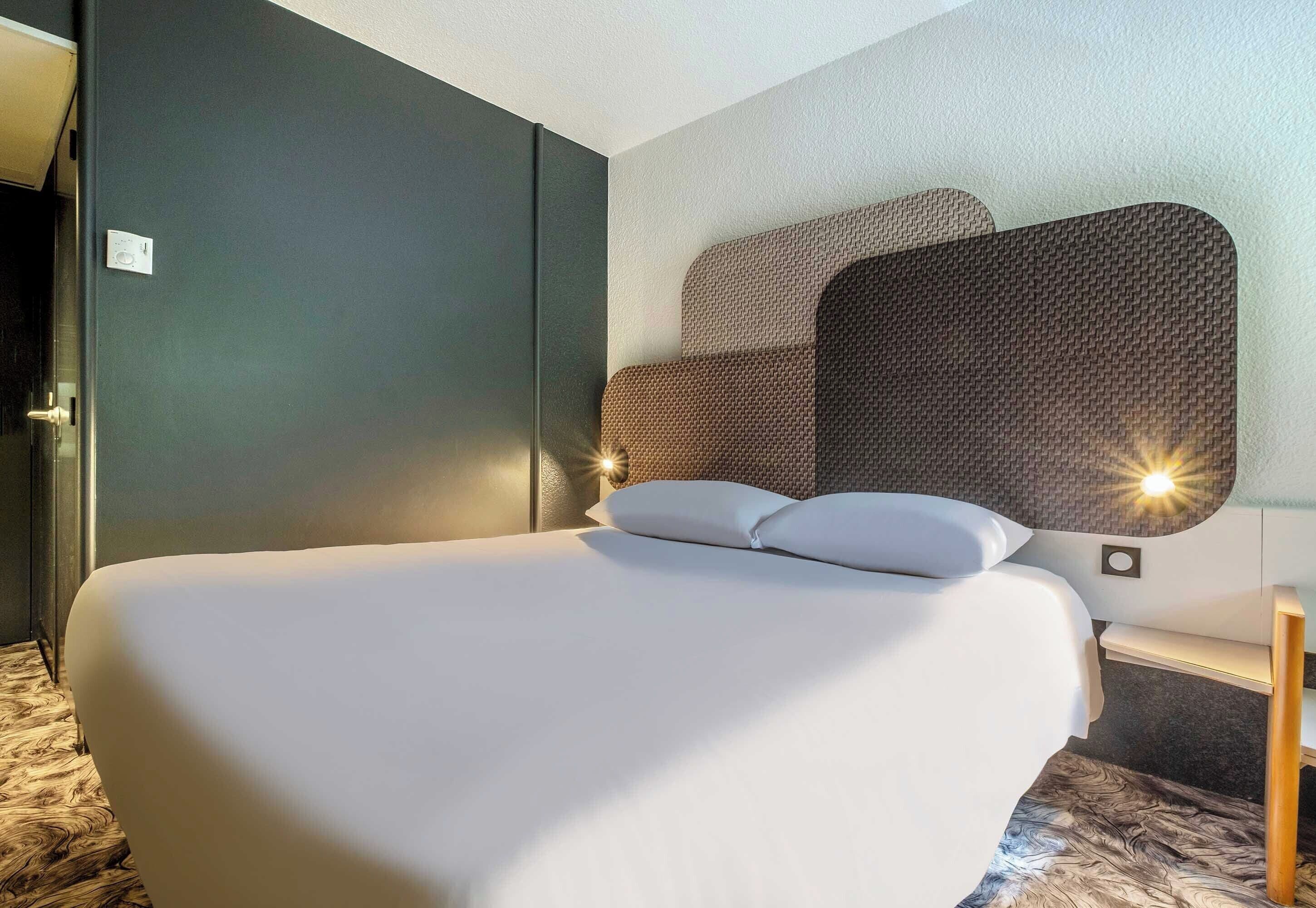 A hotel room with a large bed, a headboard with a textured design, and a bedside table with a lamp.