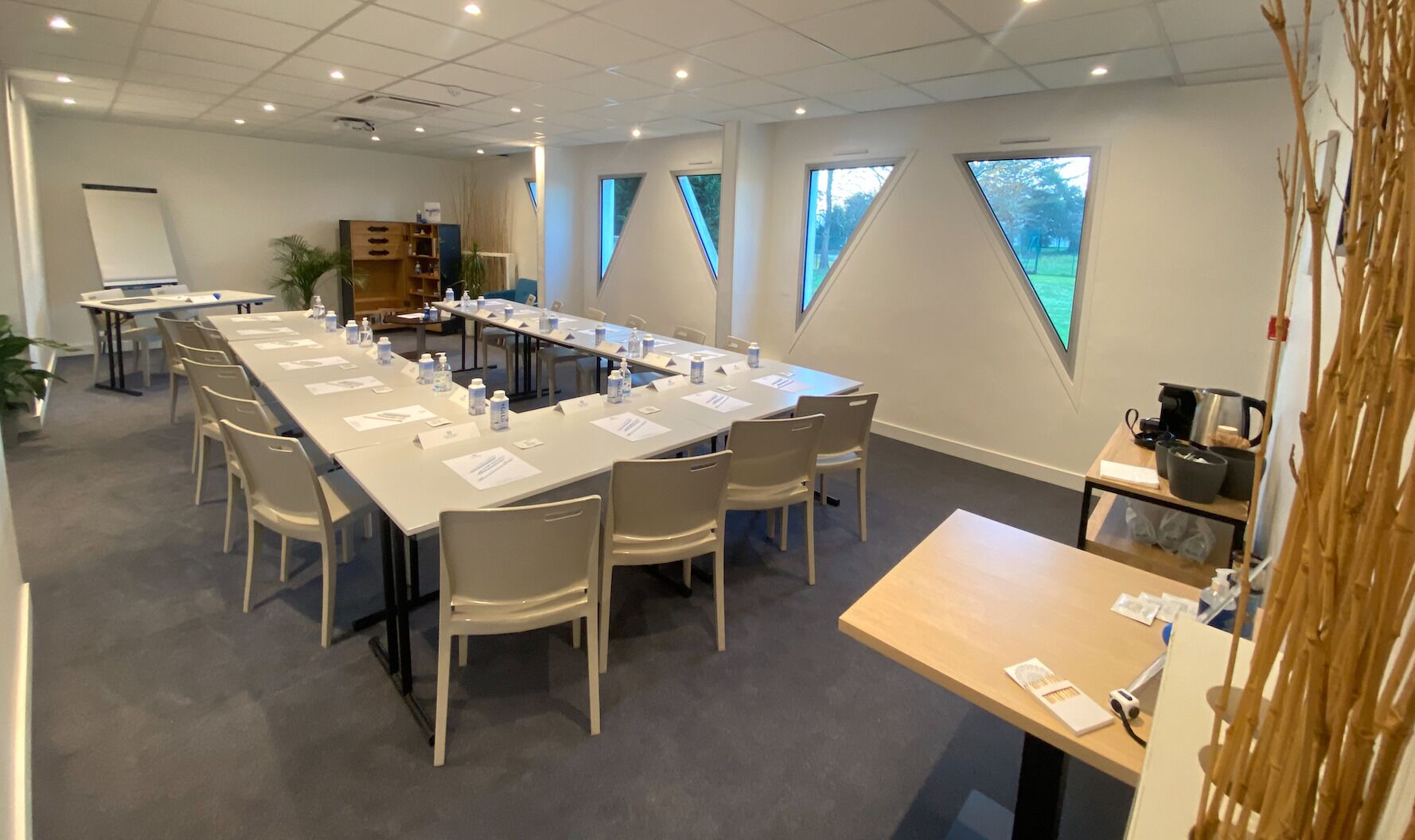 Une salle de conférence équipée d’une longue table, de chaises, d’un tableau blanc et d’un coin café.