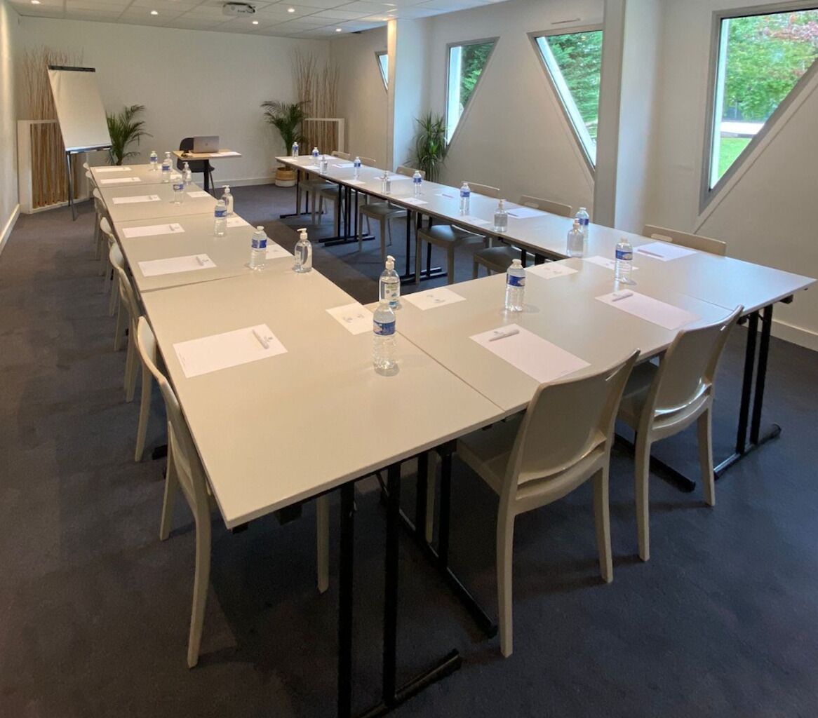 Un salón de conferencias con mesas largas, sillas, botellas de agua y una pizarra.