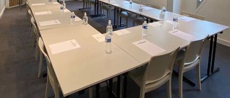 Un salón de conferencias con mesas largas, sillas, botellas de agua y una pizarra.