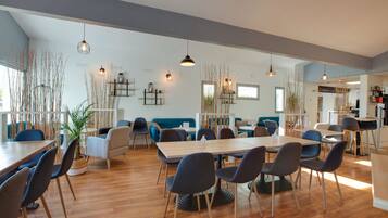 Un amplio comedor con mesas altas y sillas modernas, bañado por la luz natural y decorado con plantas de interior.