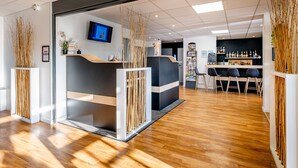 A modern reception area with a wooden floor, a reception desk, and a bar area with seating. - Sure Hotel by Best Western Bordeaux Lac (Bordeaux)