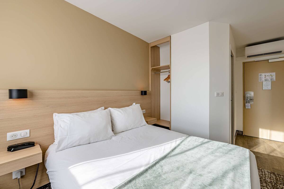 Una habitación de hotel con cama, mesita de noche y cabecero de madera.