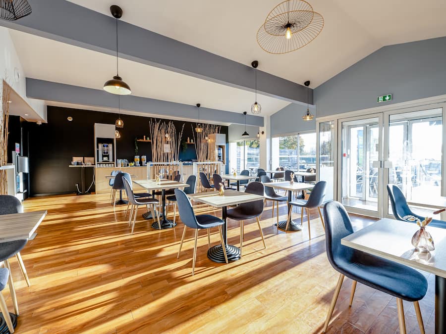 A modern dining area with wooden flooring, blue chairs, and pendant lighting.