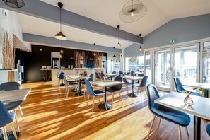Un comedor moderno con suelo de madera, sillas azules e iluminación colgante.