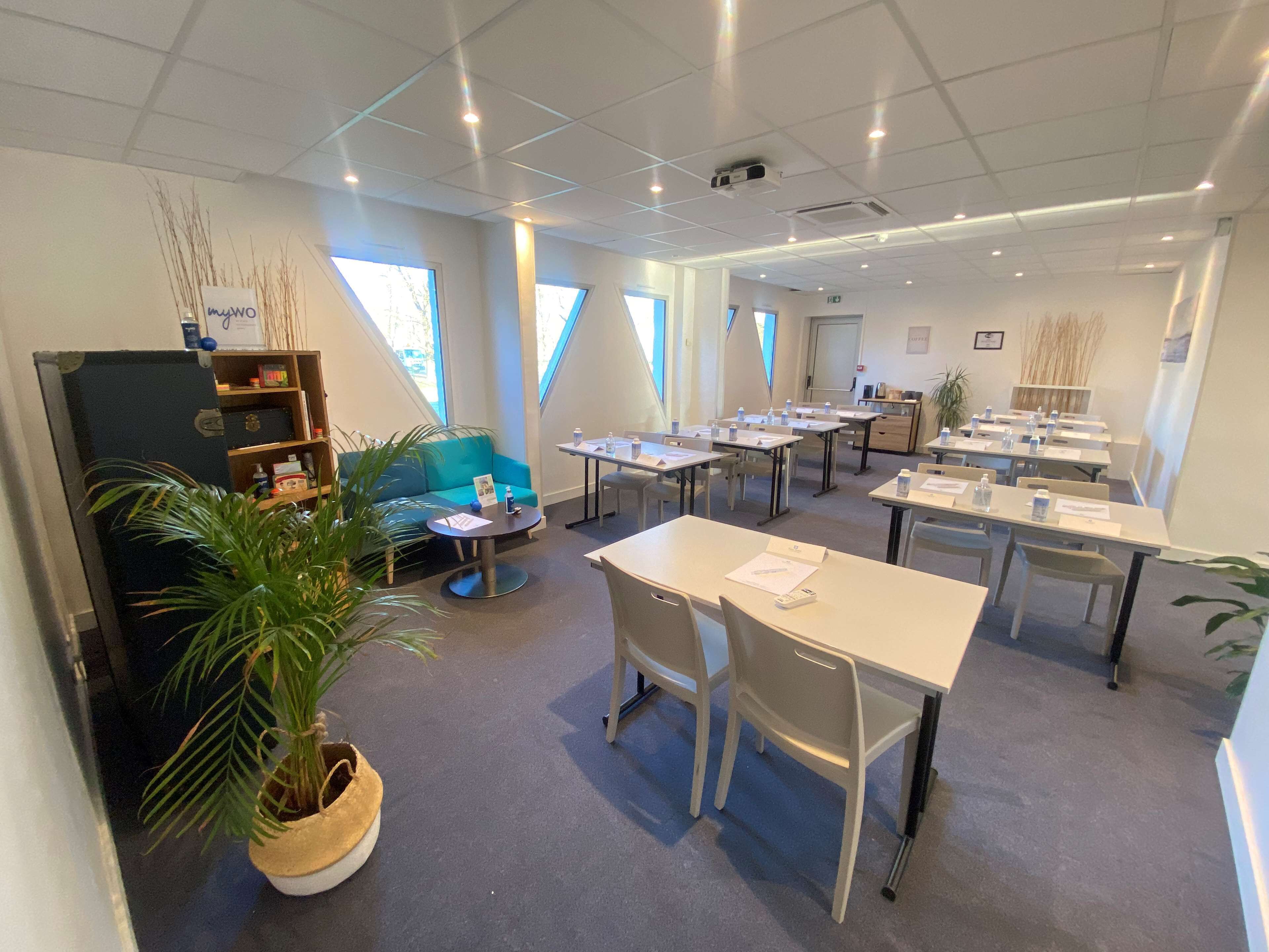 Une salle de conférence moderne, équipée de tables, de chaises et d’un canapé bleu.