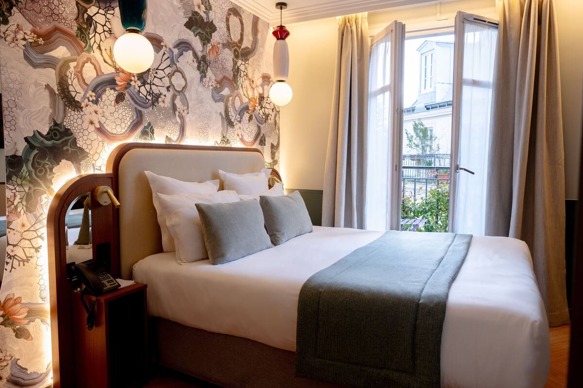 A neatly made bed with a grey blanket, a bedside telephone, and a wall with a floral pattern.