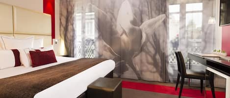 Een moderne hotelkamer met een groot bed, een bureau en uitzicht op een stadsbeeld door dunne gordijnen.