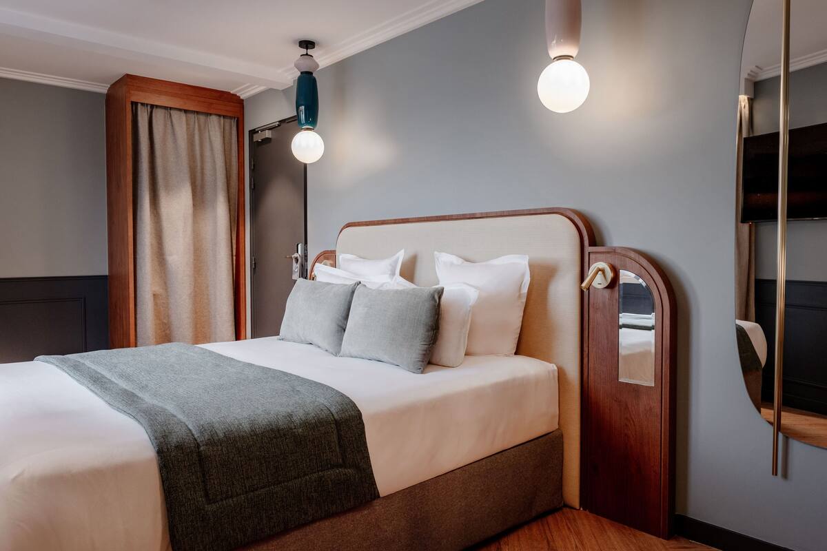 A neatly made bed with a grey blanket, a wooden headboard, and a bedside table with a mirror.