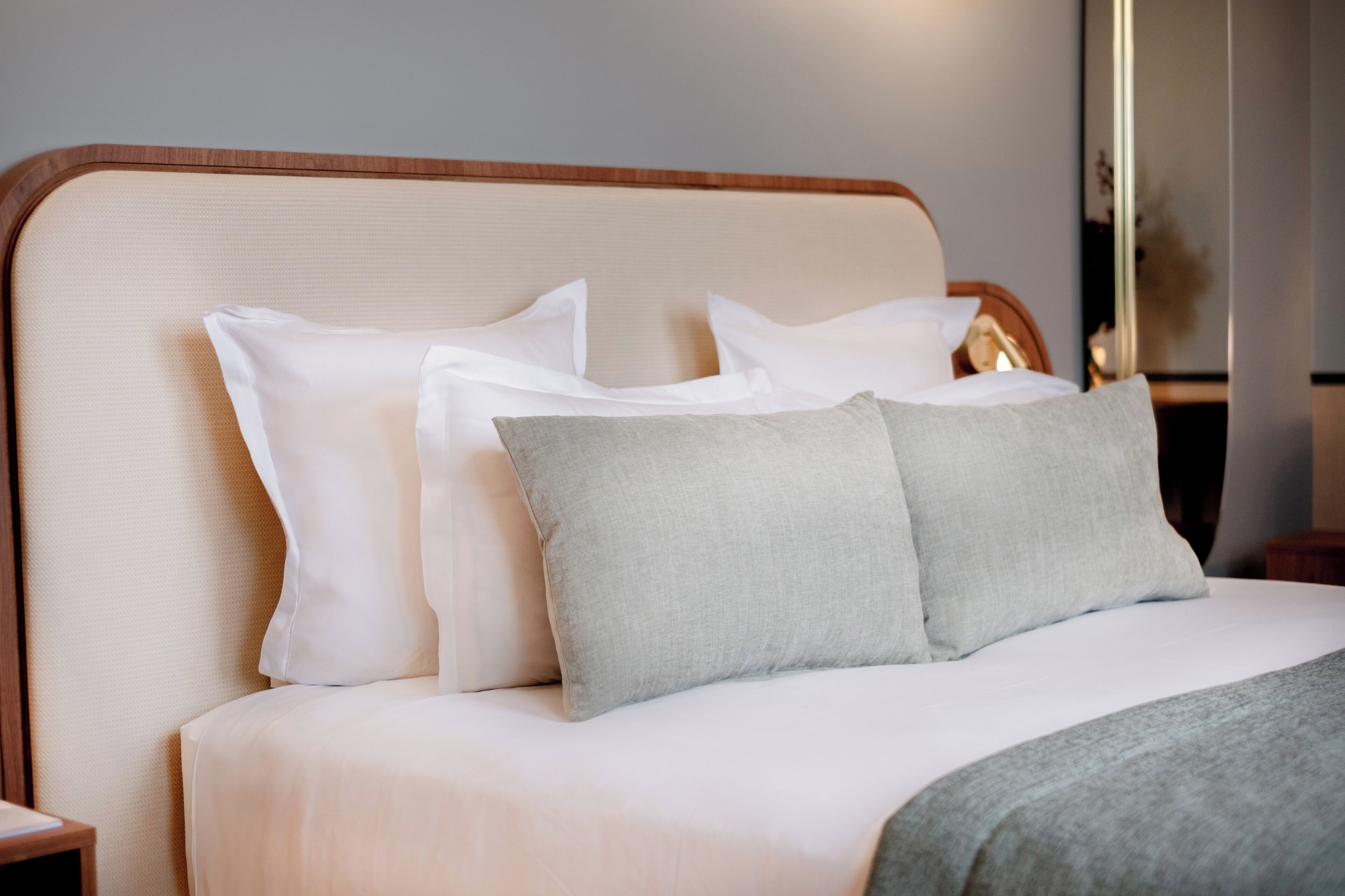 A neatly made bed with white and grey pillows, a wooden headboard, and a bedside table with a lamp.