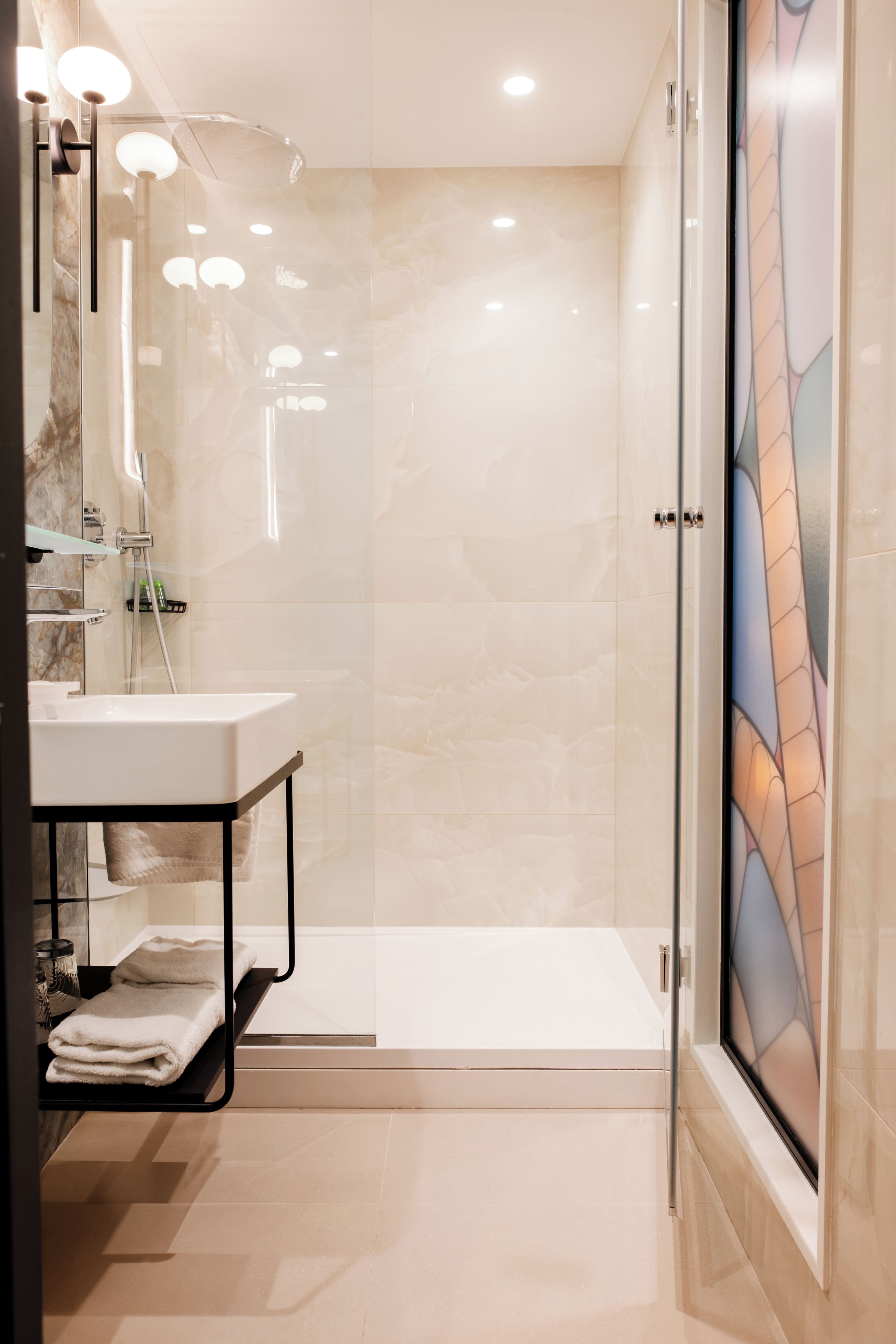 A modern bathroom with a glass shower enclosure, a white sink, and a glass door with a decorative pattern.