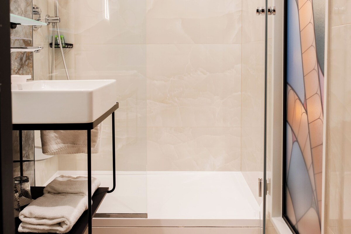 A modern bathroom with a glass shower enclosure, a white sink, and a glass door with a decorative pattern.