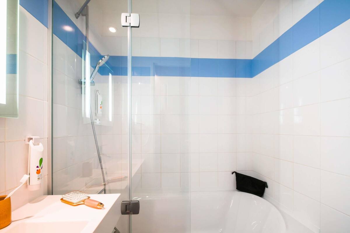 A modern bathroom with a glass shower enclosure, a white sink with a towel, and a black towel on the floor.