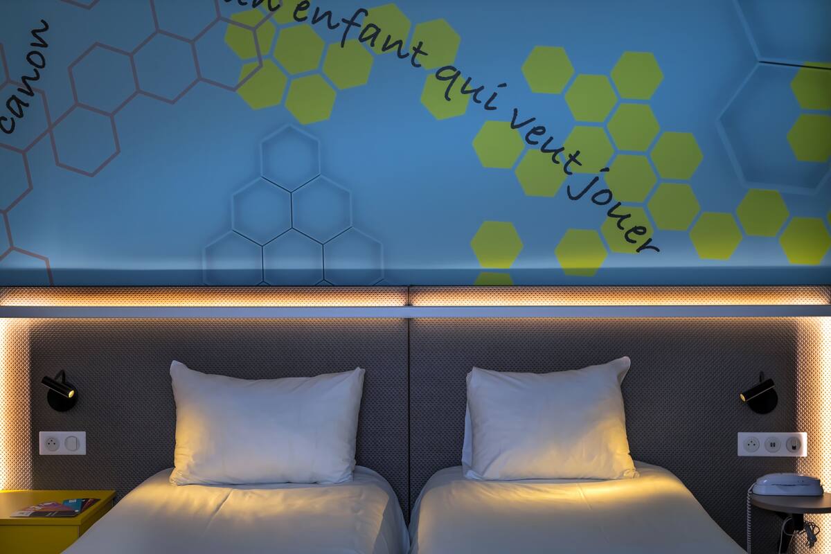 A hotel room with two beds, a wall with hexagonal patterns, and a neon sign.
