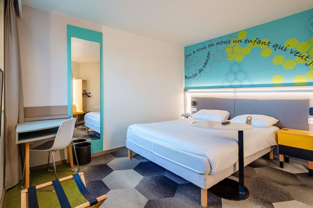 A hotel room with a bed, desk, chair, and a colorful wall mural.