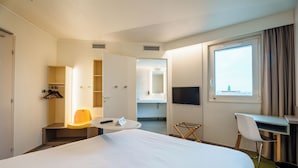 A hotel room with a large bed, a desk with a chair, a small table with a chair, a TV mounted on the wall, and a window with curtains. - ibis Styles Strasbourg Stade de la Meinau (Strasbourg)