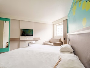 Une chambre dâhĂŽtel avec un lit, un tĂ©lĂ©viseur fixĂ© au mur, une petite table avec une tĂ©lĂ©commande, une chaise et une fenĂȘtre avec des rideaux.