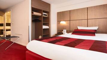 A hotel room with a large bed, a wardrobe, a bedside table, and a red carpet.