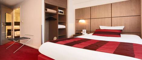 A hotel room with a large bed, a wardrobe, a bedside table, and a red carpet.
