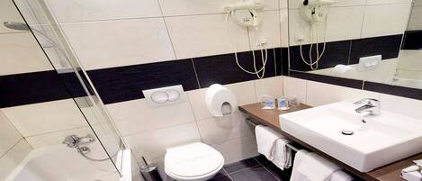 Un baño moderno con ducha envuelta en cristal, inodoro blanco, lavabo con espejo y toallero.