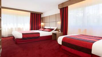 Habitación de hotel con dos camas, cortinas rojas, cabecera de madera y un ventanal grande.