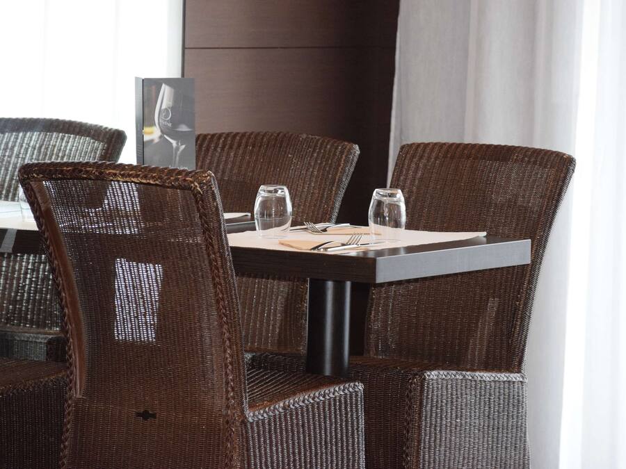 Un coin repas avec des chaises en osier et une table dressée pour deux personnes, agrémentée d’un verre à vin et d’un verre à eau.