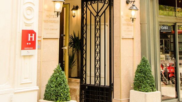 L’entrée d’un hôtel, avec une enseigne indiquant « HÔTEL PARIS BRUXELLES » et un panneau en forme de « H » signalant l’hôtel.