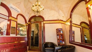 Un hall d’hôtel comprenant un comptoir d’accueil, un lustre, un fauteuil en cuir et une bibliothèque.