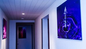 Un couloir dont le plafond est doté d’un éclairage encastré et où l’on peut admirer, sur le mur de droite, une grande peinture abstraite.