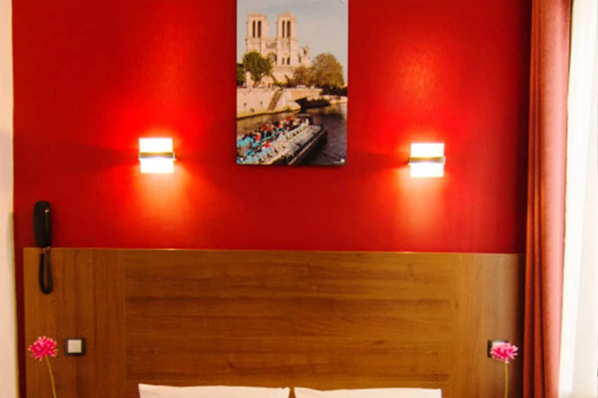 A hotel room with a wooden headboard, white bedding, and a red accent wall.