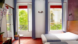 Une chambre d’hôtel avec deux lits, une petite table ronde, un miroir et une fenêtre avec des rideaux.