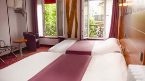 Une chambre d’hôtel avec deux lits, une petite table, une chaise et une fenêtre donnant sur l’extérieur.