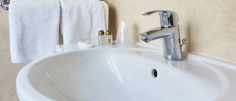 Une salle de bain avec un lavabo blanc, un robinet chromé et deux serviettes blanches suspendues à un porte-serviettes.