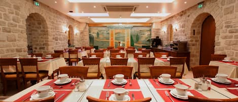 A dining area with multiple tables and chairs, stone walls, and a mural on the back wall.