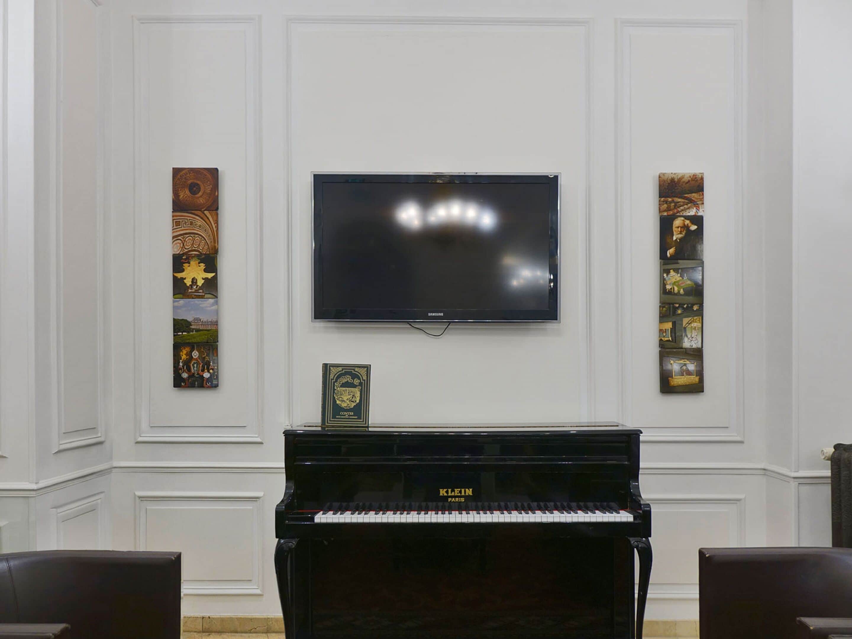Una habitación con un piano negro, un televisor de pantalla plana y dos cuadros verticales en las paredes.
