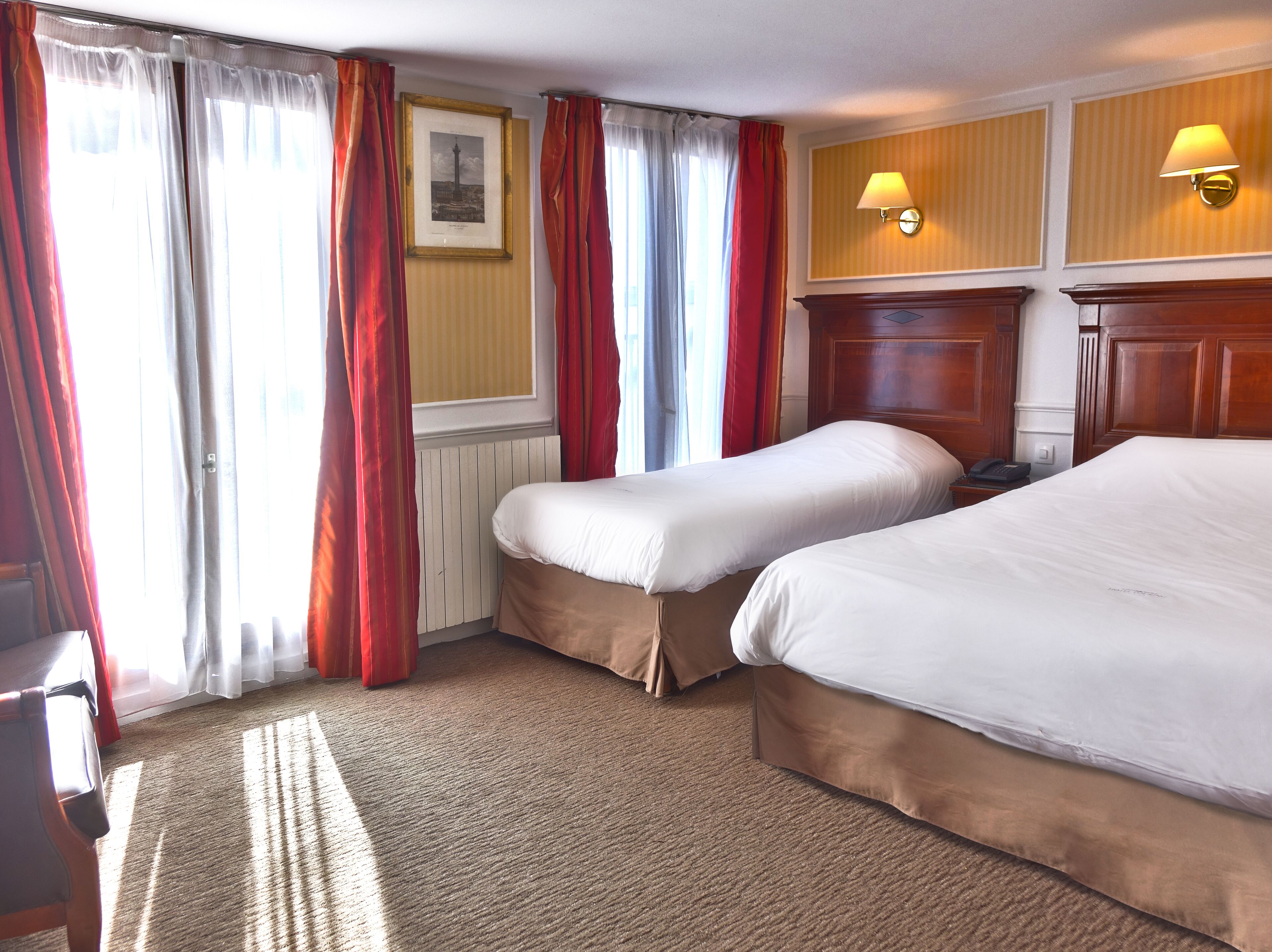 A hotel room with two beds, a wooden headboard, a framed picture on the wall, and a carpeted floor.