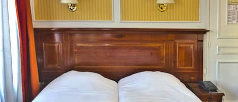 A double bed with a wooden headboard, two wall-mounted lamps, and a telephone on a bedside table.