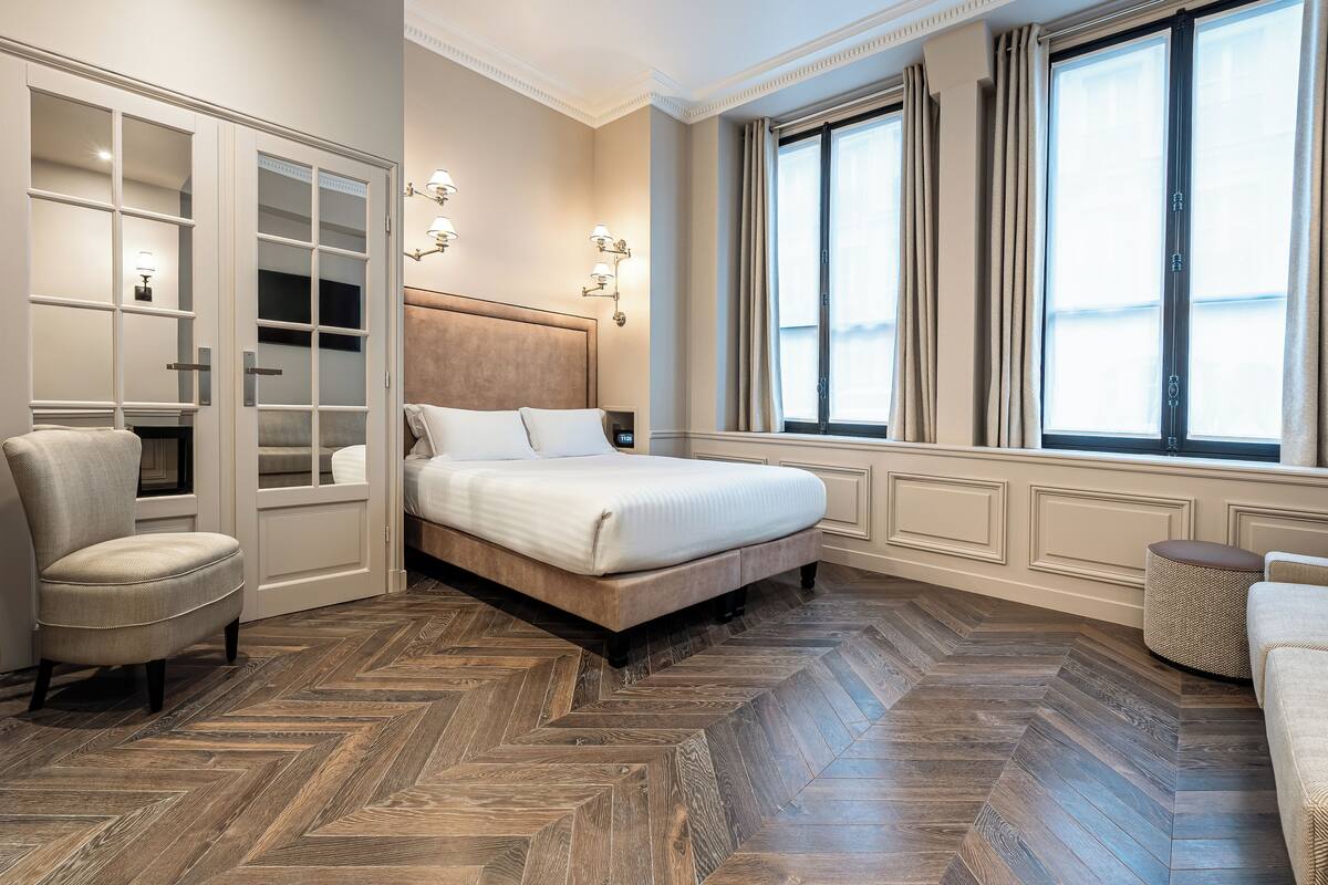 A bedroom with a large bed, a wardrobe, a chair, and a window with curtains.